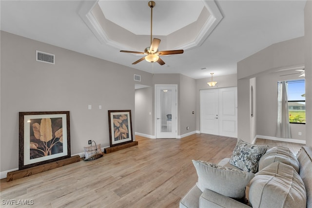 living room featuring a raised ceiling, ceiling fan, and light wood-type flooring