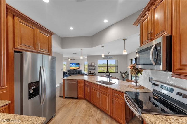 kitchen with hanging light fixtures, light stone counters, stainless steel appliances, light hardwood / wood-style floors, and sink