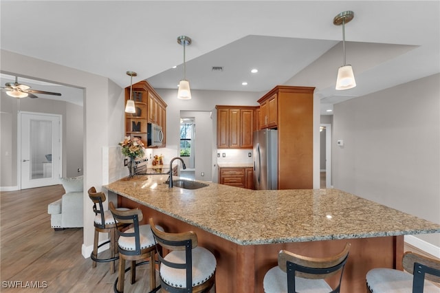 kitchen featuring hardwood / wood-style flooring, appliances with stainless steel finishes, kitchen peninsula, ceiling fan, and a breakfast bar