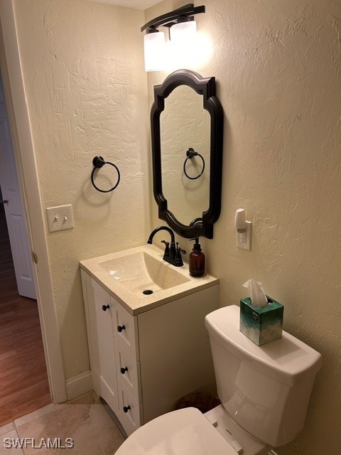 half bathroom with toilet, vanity, and a textured wall