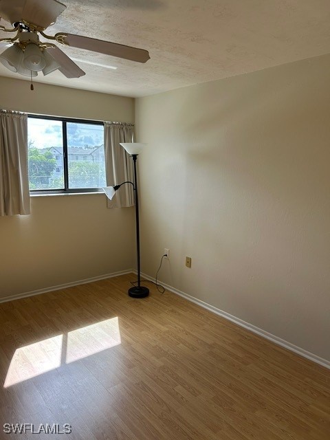 unfurnished room featuring wood finished floors, a textured ceiling, baseboards, and ceiling fan