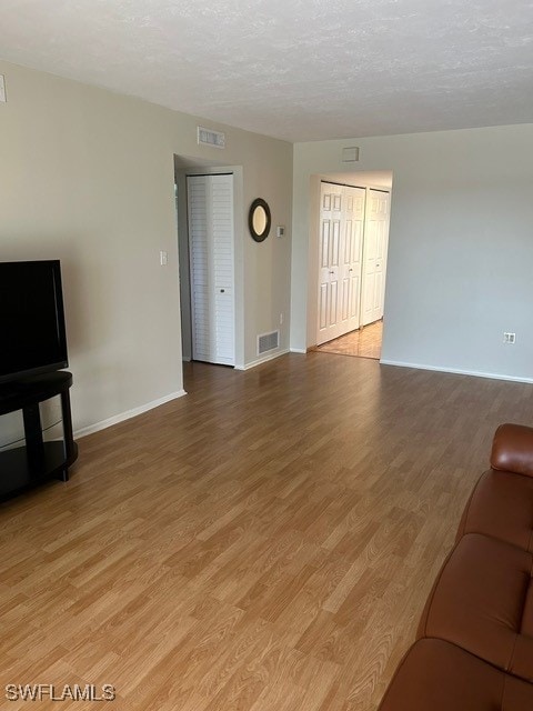 unfurnished living room with a textured ceiling, baseboards, light wood-style flooring, and visible vents