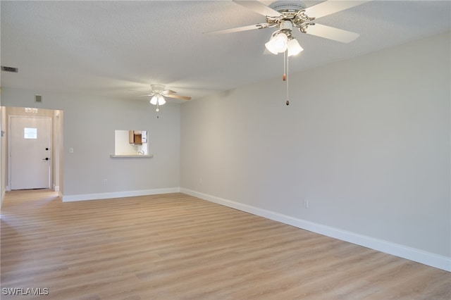 spare room featuring visible vents, baseboards, light wood-style floors, a textured ceiling, and a ceiling fan