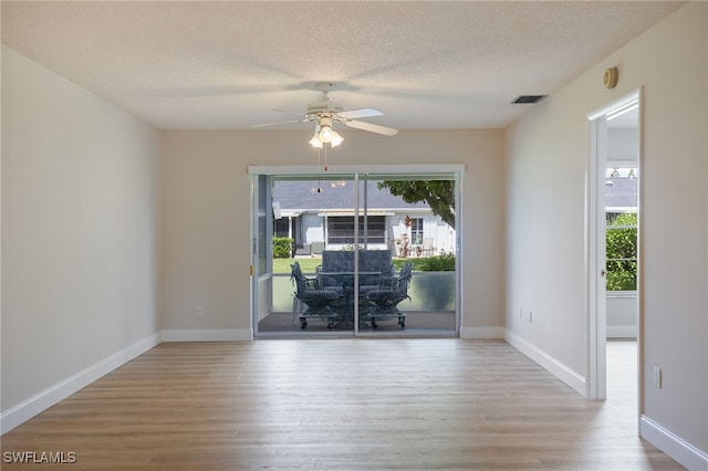 empty room with a textured ceiling, light wood-type flooring, baseboards, and a healthy amount of sunlight