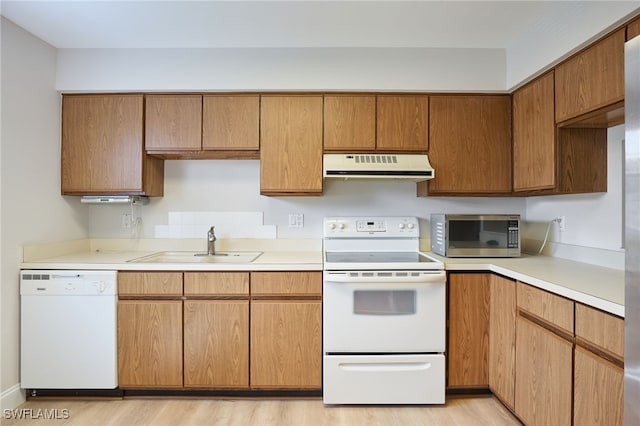 kitchen featuring light countertops, brown cabinetry, a sink, white appliances, and under cabinet range hood