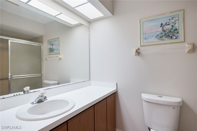 bathroom with toilet, a skylight, a shower with door, and vanity