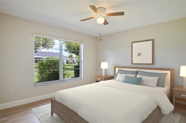 bedroom with ceiling fan, a textured ceiling, baseboards, and wood finished floors