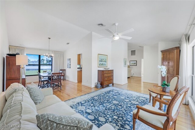 living room featuring ceiling fan with notable chandelier, vaulted ceiling, and light hardwood / wood-style flooring