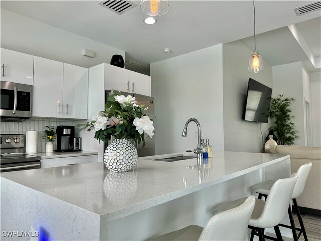 kitchen with tasteful backsplash, decorative light fixtures, sink, appliances with stainless steel finishes, and white cabinets