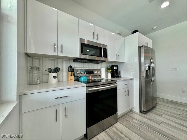 kitchen featuring white cabinetry, stainless steel appliances, decorative backsplash, and light hardwood / wood-style floors