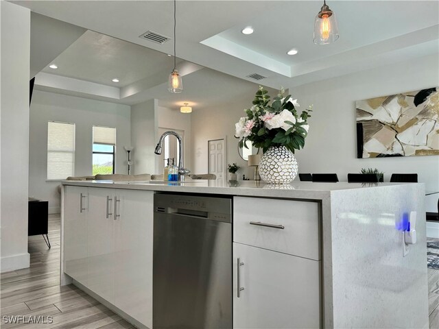 kitchen with a raised ceiling, dishwasher, pendant lighting, light hardwood / wood-style flooring, and white cabinets