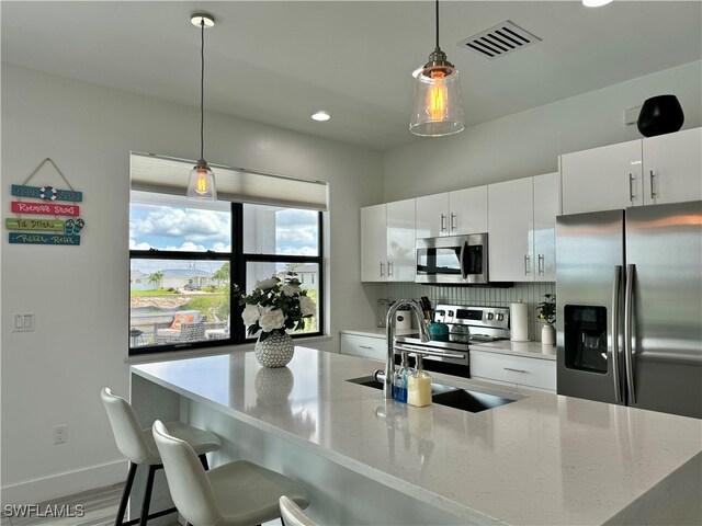 kitchen with appliances with stainless steel finishes, hanging light fixtures, sink, decorative backsplash, and white cabinetry