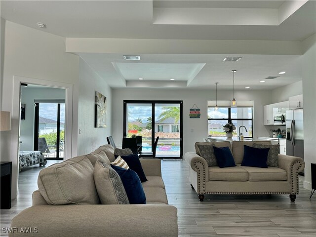 living room with a tray ceiling, sink, and light hardwood / wood-style floors