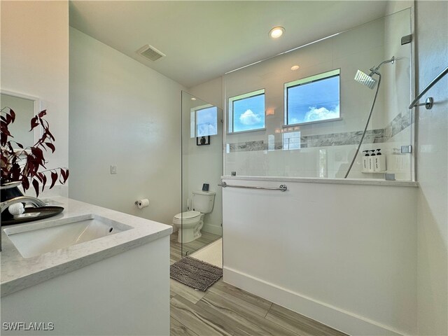 bathroom featuring vanity, toilet, a tile shower, and hardwood / wood-style floors