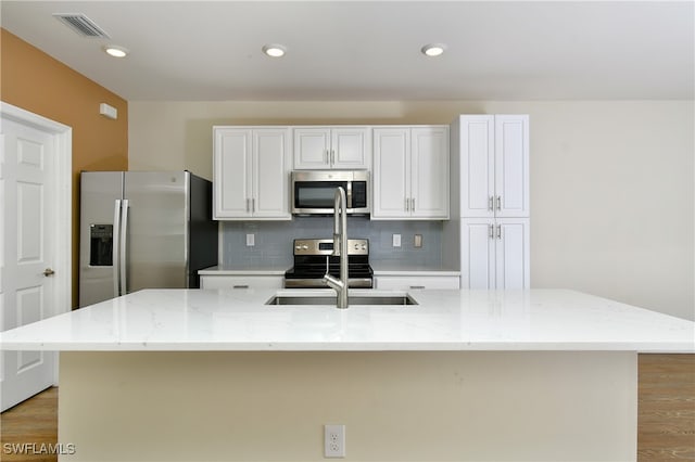 kitchen featuring a center island with sink, stainless steel appliances, light stone counters, and light wood-type flooring