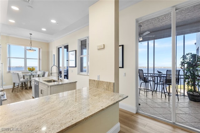 kitchen featuring a water view, hanging light fixtures, white cabinets, a sink, and an island with sink