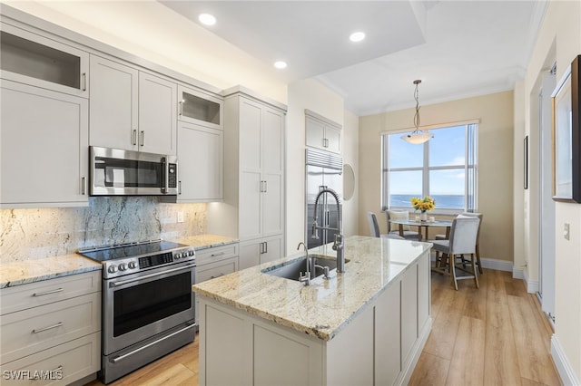 kitchen with a kitchen island with sink, decorative light fixtures, appliances with stainless steel finishes, light stone countertops, and glass insert cabinets