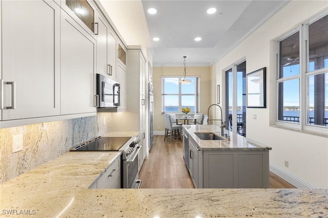 kitchen featuring appliances with stainless steel finishes, decorative light fixtures, a sink, and light stone counters