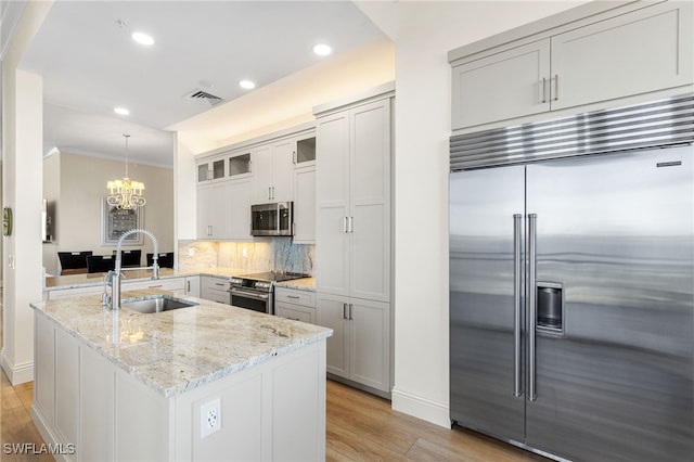 kitchen with glass insert cabinets, light stone counters, stainless steel appliances, pendant lighting, and a sink