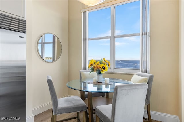 dining space featuring a water view, light wood-type flooring, and baseboards