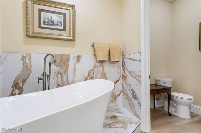 full bathroom with a freestanding tub, wainscoting, toilet, and wood finished floors