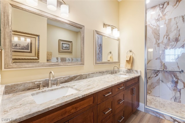 bathroom with wood finished floors, a sink, a marble finish shower, and double vanity