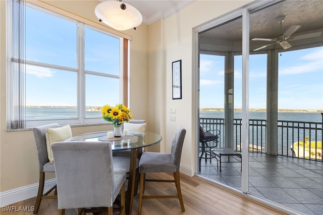 dining area with hardwood / wood-style flooring, crown molding, a water view, and ceiling fan