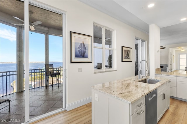 kitchen with a water view, stainless steel dishwasher, white cabinetry, ceiling fan, and a sink