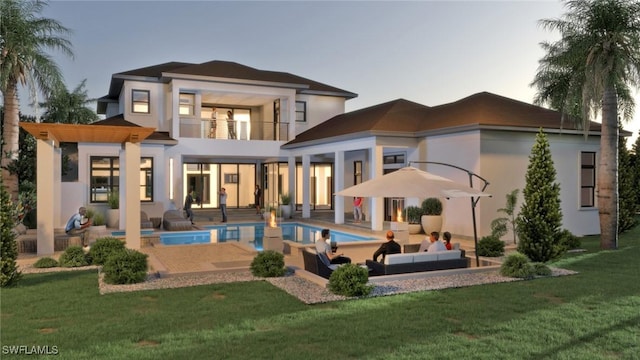 back house at dusk with a patio area, outdoor lounge area, a balcony, and a lawn