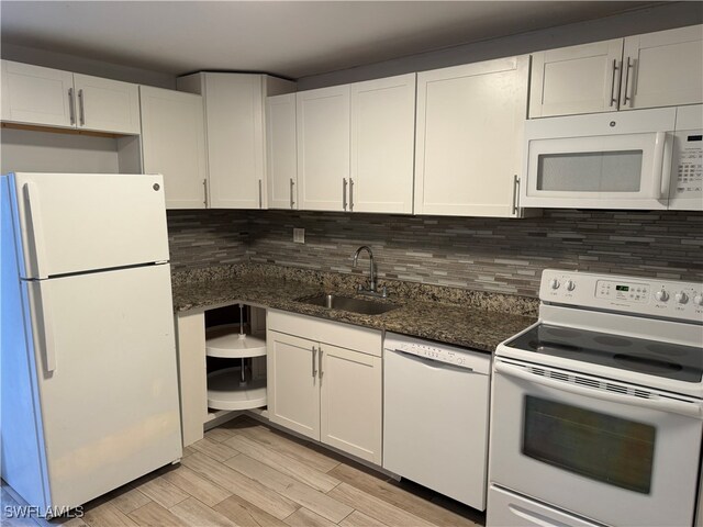 kitchen featuring light wood-type flooring, dark stone countertops, white appliances, sink, and white cabinets