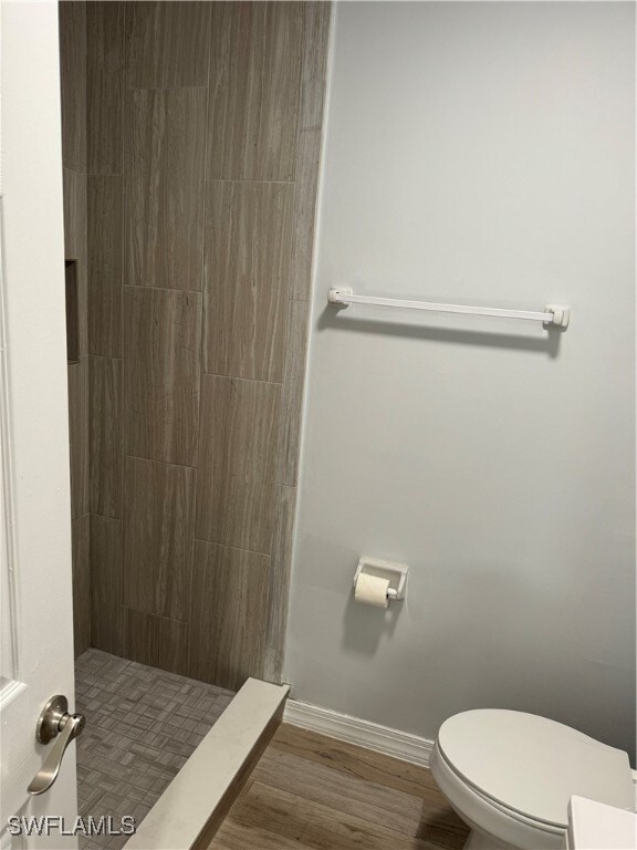 bathroom with tiled shower, toilet, and hardwood / wood-style flooring