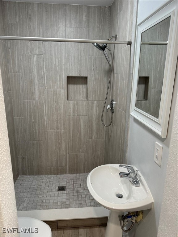 bathroom with tiled shower, toilet, and wood-type flooring