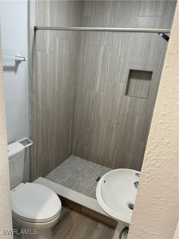 bathroom with toilet, a tile shower, and wood-type flooring