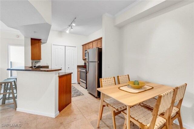 kitchen with light tile patterned floors, appliances with stainless steel finishes, dark stone counters, kitchen peninsula, and ornamental molding