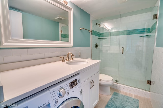 bathroom with a shower with door, tile walls, toilet, and vanity