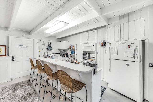 kitchen featuring beamed ceiling, a kitchen bar, white appliances, and white cabinetry