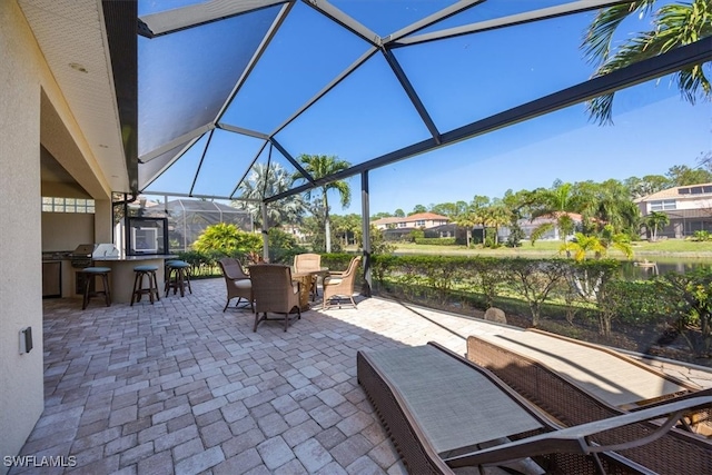 view of patio with area for grilling, exterior bar, a water view, and glass enclosure