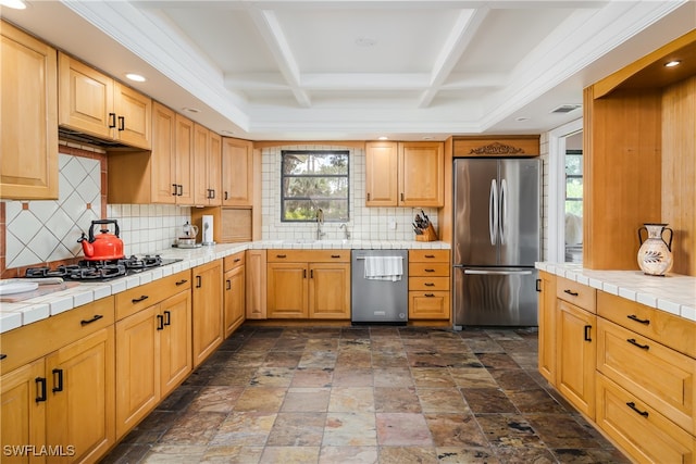 kitchen featuring tile counters, coffered ceiling, appliances with stainless steel finishes, and decorative backsplash