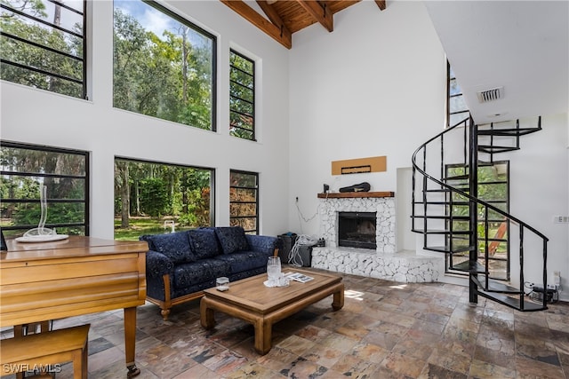 living room featuring beamed ceiling, high vaulted ceiling, and a stone fireplace