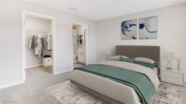 bedroom featuring light carpet, a walk in closet, ensuite bathroom, and a closet