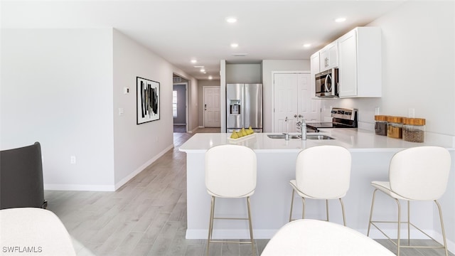 kitchen featuring kitchen peninsula, appliances with stainless steel finishes, a kitchen bar, sink, and light hardwood / wood-style flooring