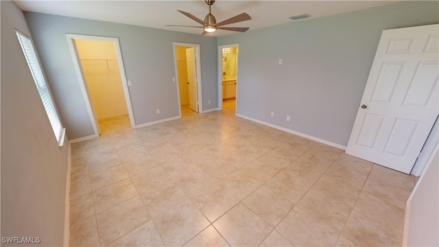 unfurnished bedroom with light tile patterned floors, ensuite bath, a closet, a spacious closet, and ceiling fan