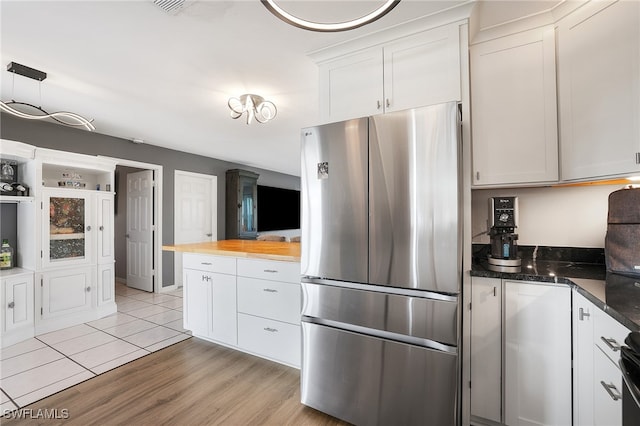 kitchen featuring dark stone countertops, pendant lighting, stainless steel fridge, light tile patterned floors, and white cabinets