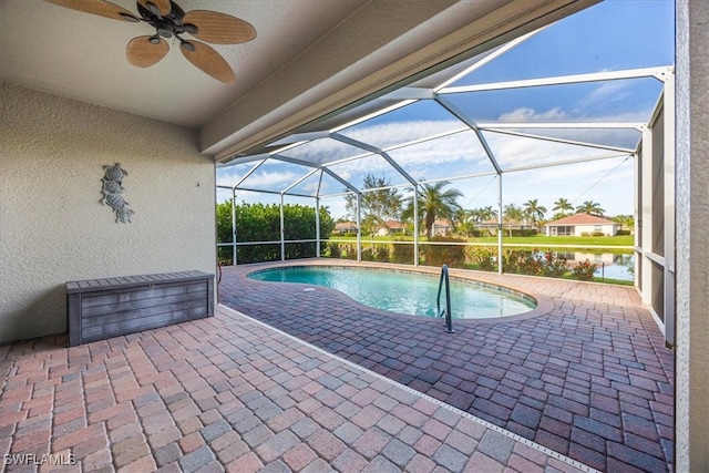 view of swimming pool with glass enclosure, ceiling fan, a patio area, and a water view