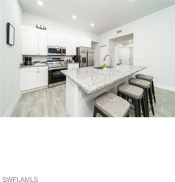 kitchen featuring sink, a kitchen island with sink, white cabinetry, stainless steel appliances, and a breakfast bar area