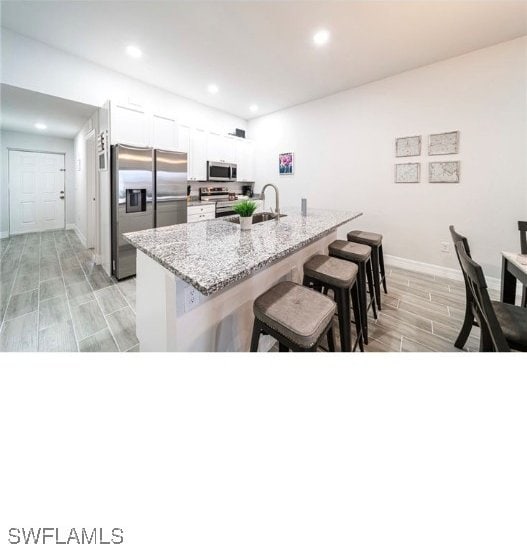 kitchen with white cabinets, light stone countertops, appliances with stainless steel finishes, a kitchen breakfast bar, and light wood-type flooring