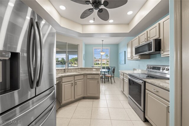 kitchen featuring stainless steel appliances, decorative light fixtures, a raised ceiling, and light stone countertops