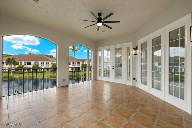 unfurnished sunroom with a water view, ceiling fan, and french doors