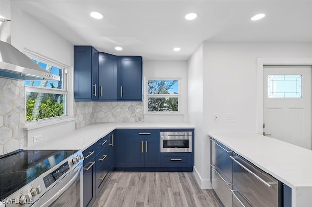 kitchen featuring a wealth of natural light, light countertops, electric range, wall chimney range hood, and a peninsula