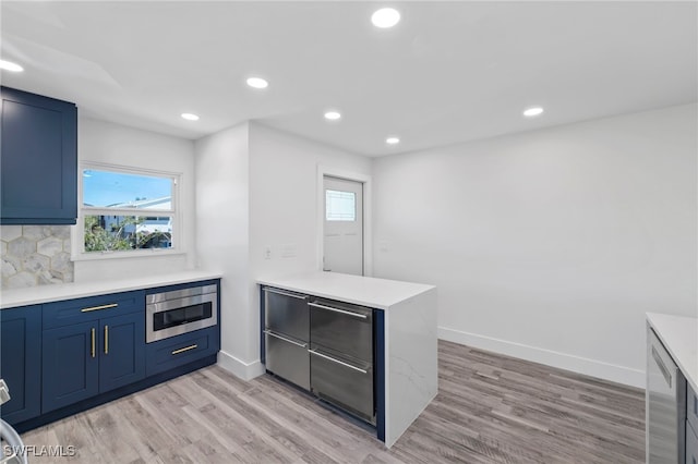 kitchen with light countertops, stainless steel microwave, a peninsula, and light wood finished floors